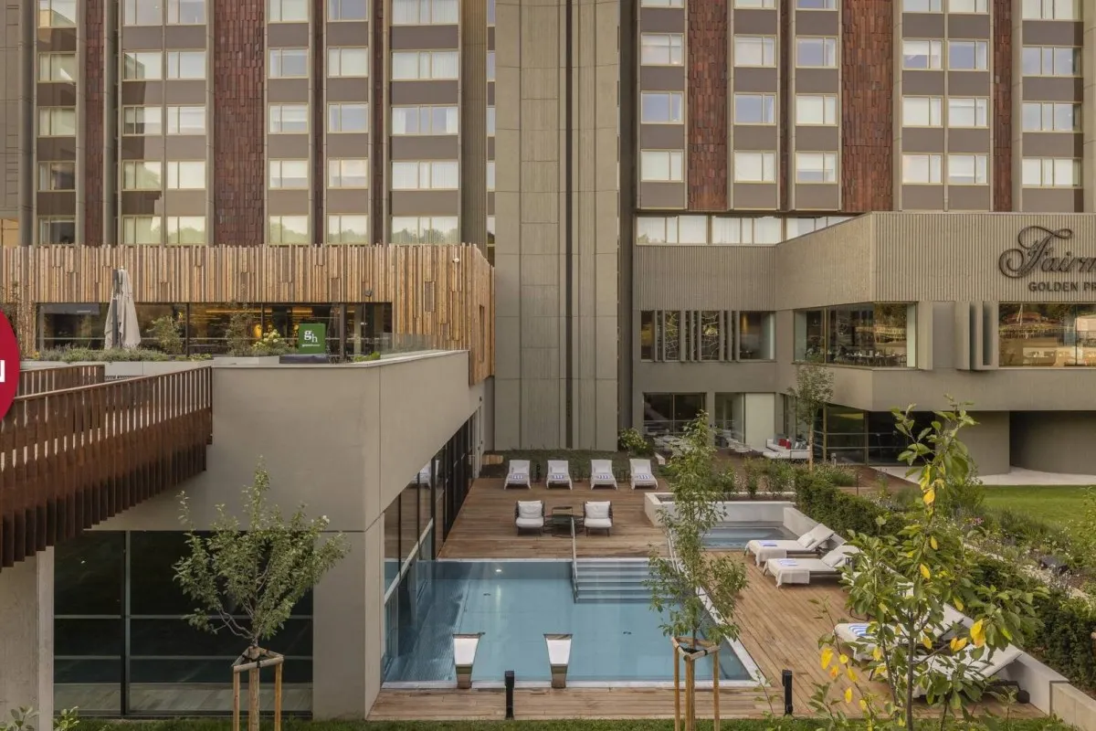 Exterior of Fairmont Golden Prague hotel with pool, sun loungers and terrace, building façade visible with hotel sign.