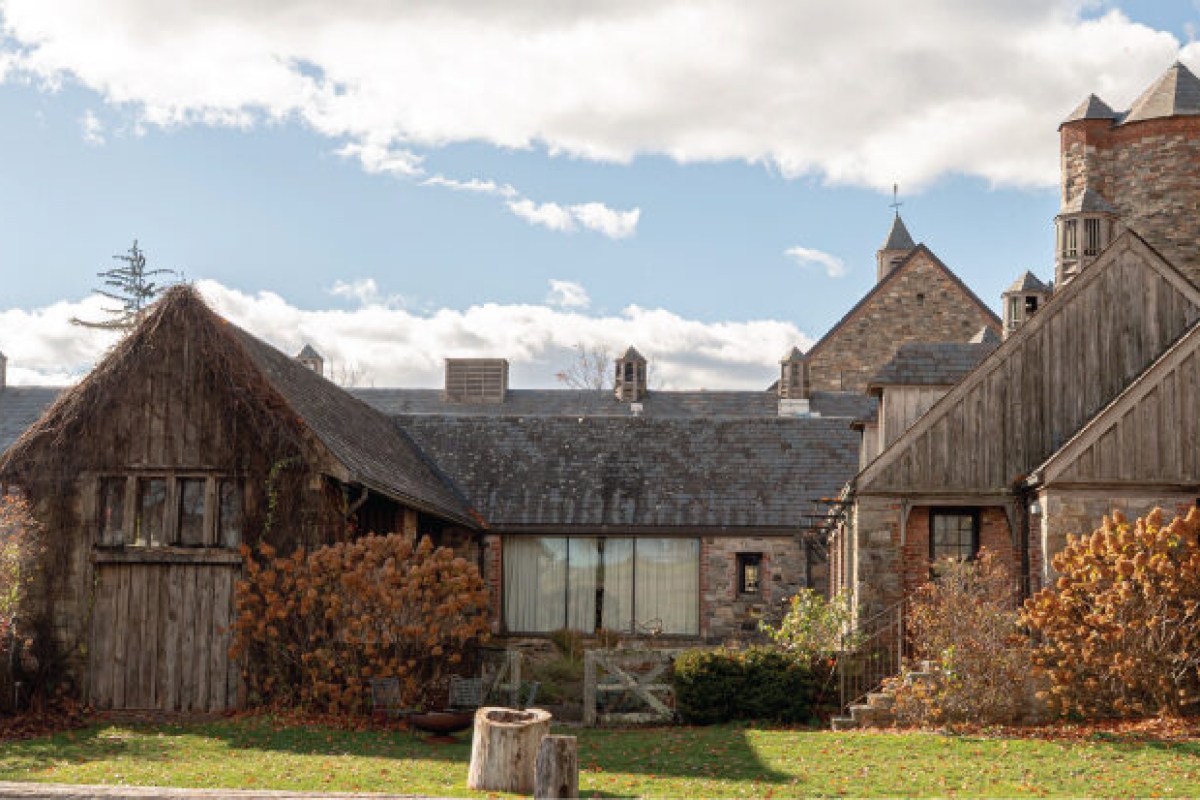 Exterior view of the stone and weathered-wood farm buildings at Blue Hill, with a large barn window and chimneys against a blue sky.