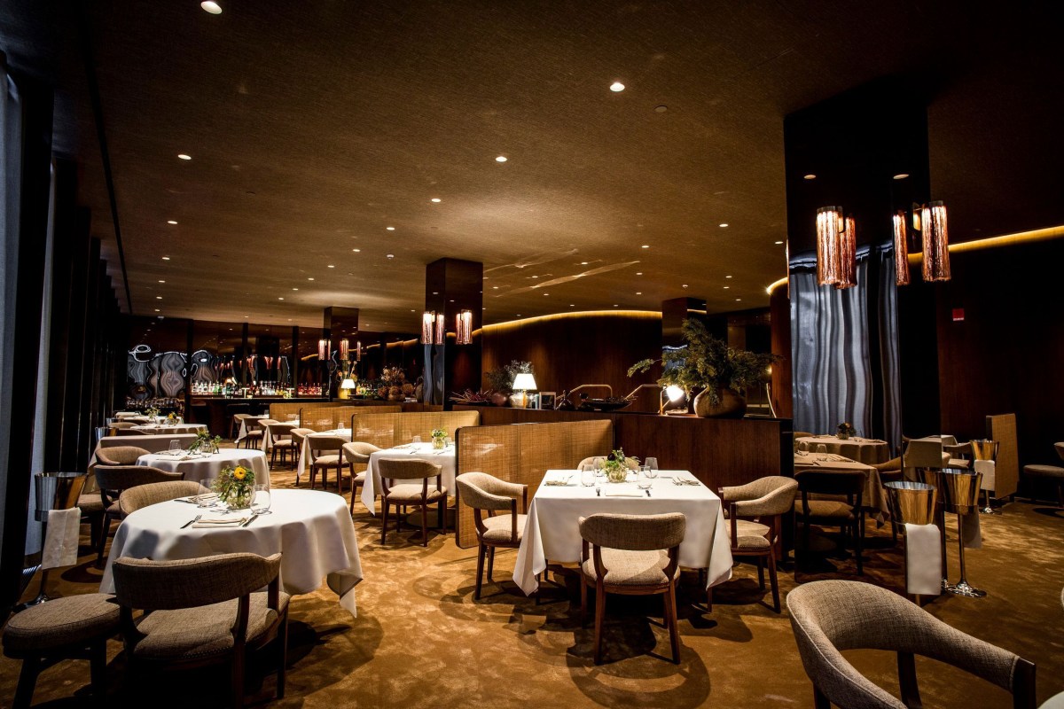 Main dining room with set tables, warm lighting, and bar in background