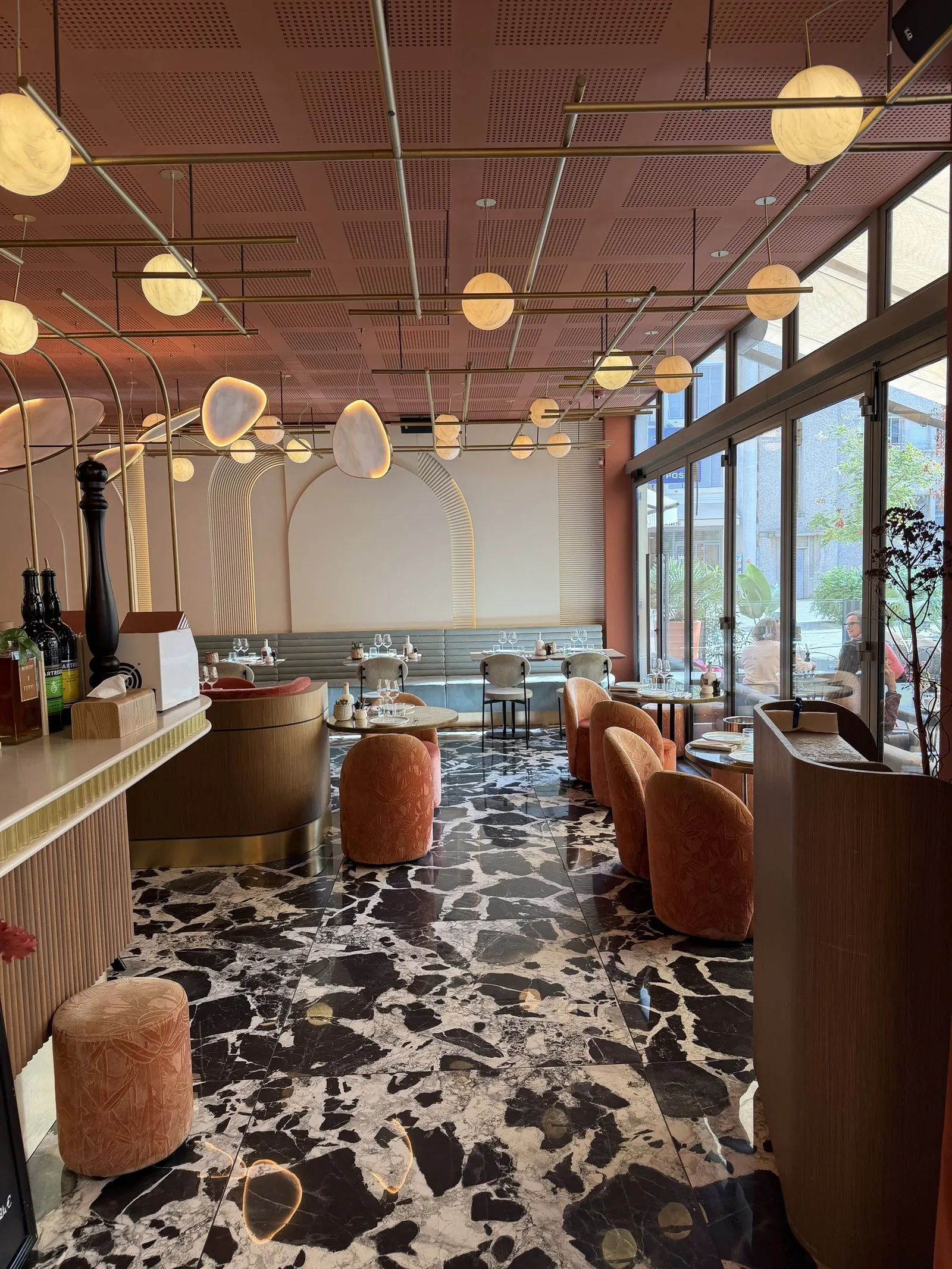 The bar and window tables at Ferni in Antibes, with globe lights under a terracotta ceiling and orange velvet chairs on marble
