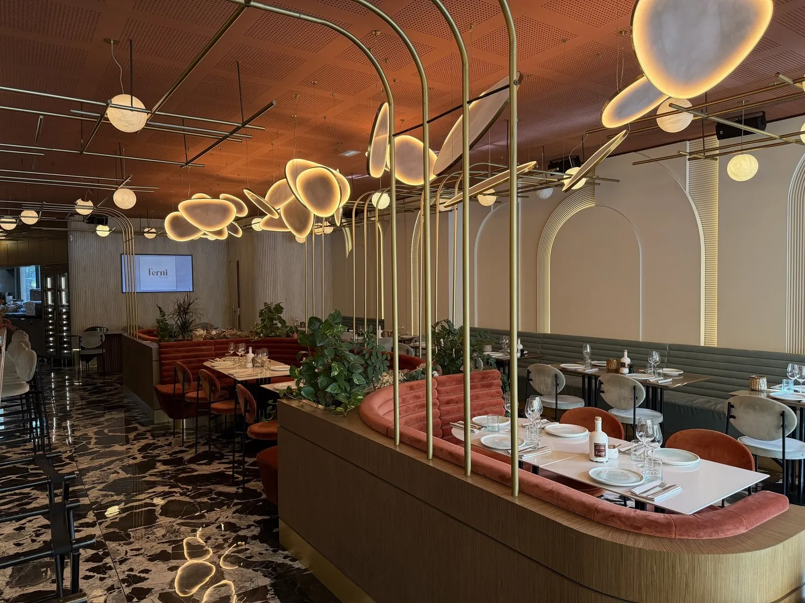 The dining room of Ferni in Antibes, with brass arches, glowing pebble-shaped lights, terracotta velvet banquettes and a black-and-white marble floor