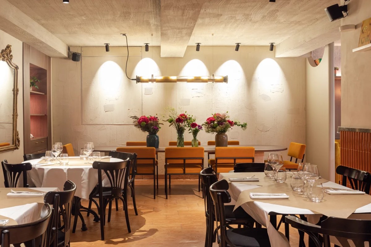 Restaurant dining room with round tables set in white linen, mustard chairs, concrete ceiling and floral centerpieces