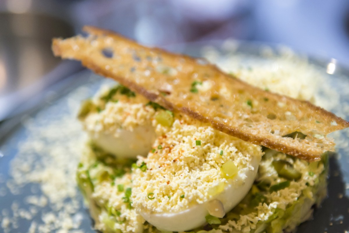 Close-up of a cheese and herb crusted dish with a crisp bread shard on top, served on a dark plate