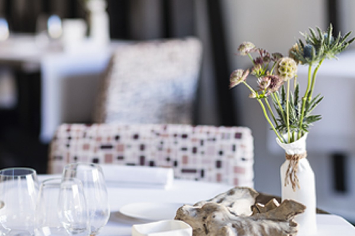 Close-up of a set table with wine glasses, white tablecloth and a vase of wildflowers