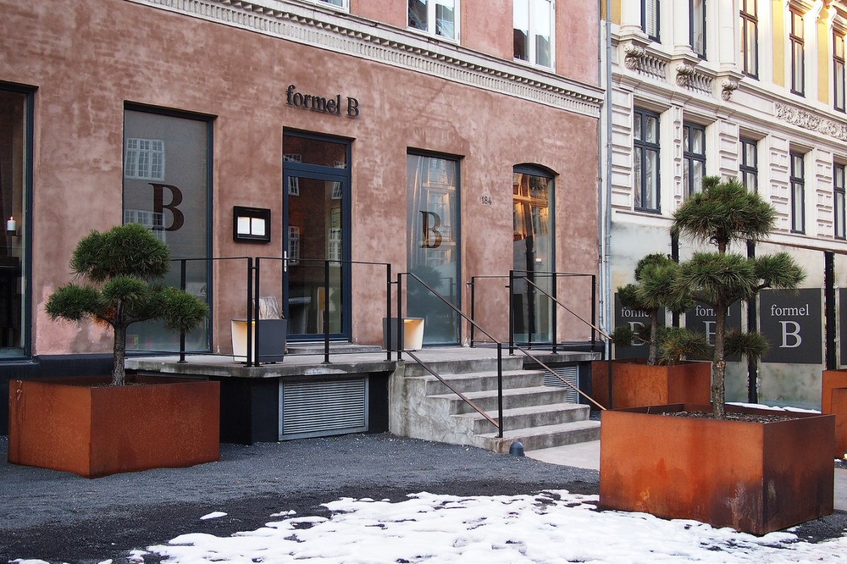 Exterior facade of Formel B restaurant with pink-toned building, bonsai trees in planters, and entrance steps, snow on ground.