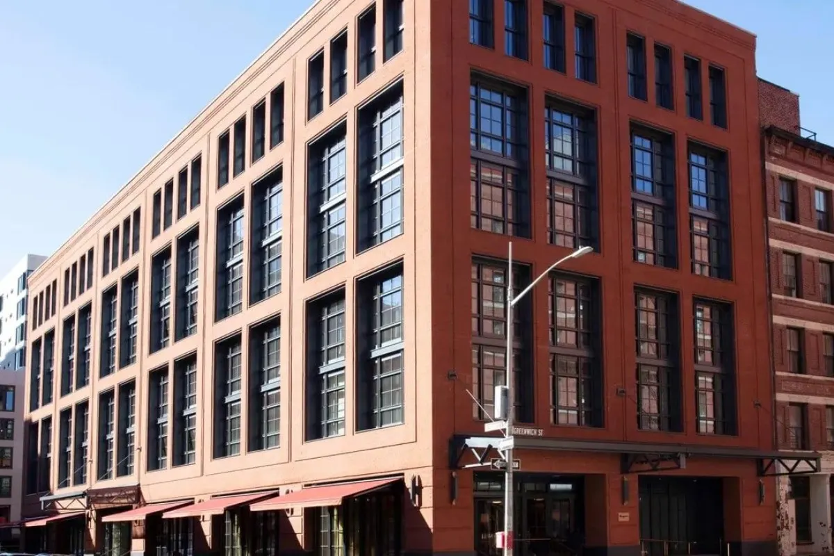 Street view of the red-brick multi-story facade of Fouquet's New York hotel on a corner, large windows and awnings.
