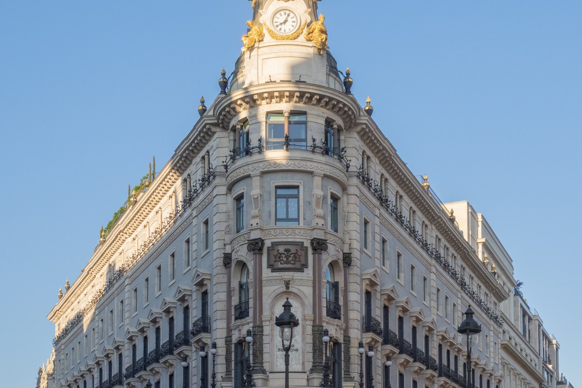 Low-angle view of the ornate corner facade and clock tower of Four Seasons Hotel Madrid against a blue sky