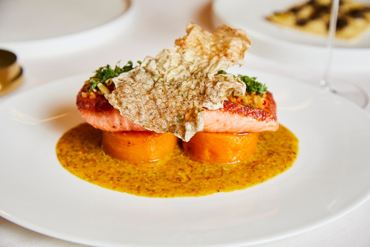 Plated salmon fillet with crispy skin garnish over orange puree and a drizzle of sauce.