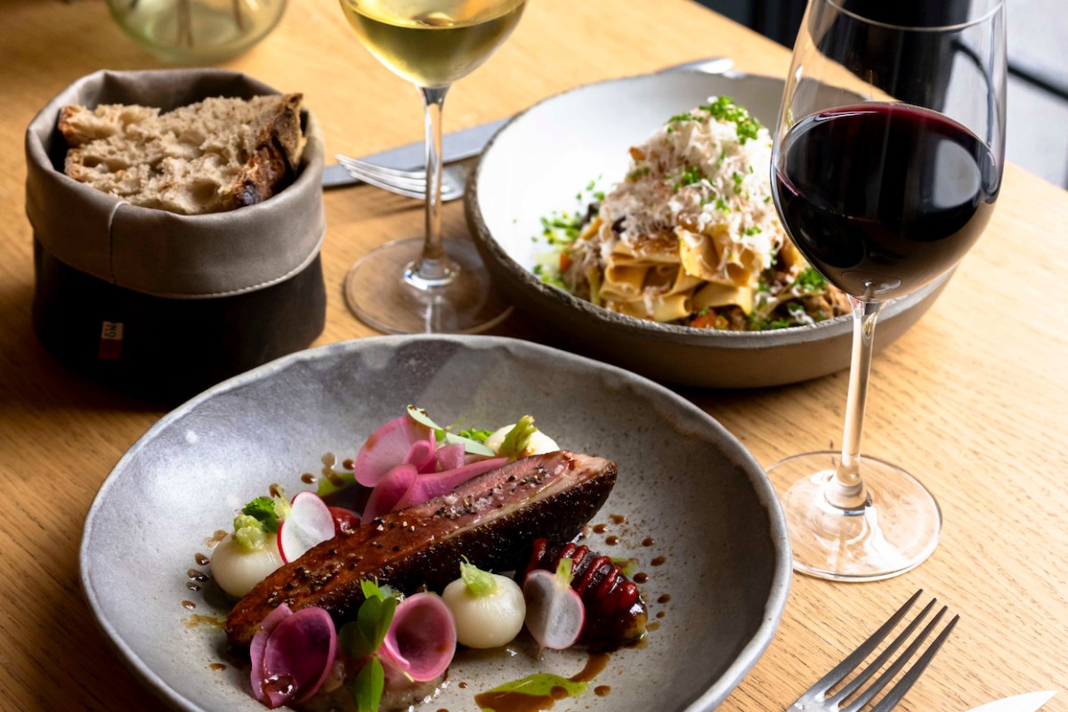 Laid table with duck breast dish, pasta bowl, bread, and glasses of red and white wine