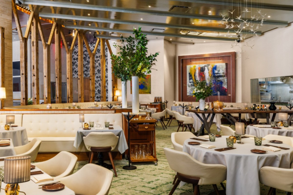 Elegant restaurant dining room with white tufted banquettes, round tables, wood beam accents, and modern art