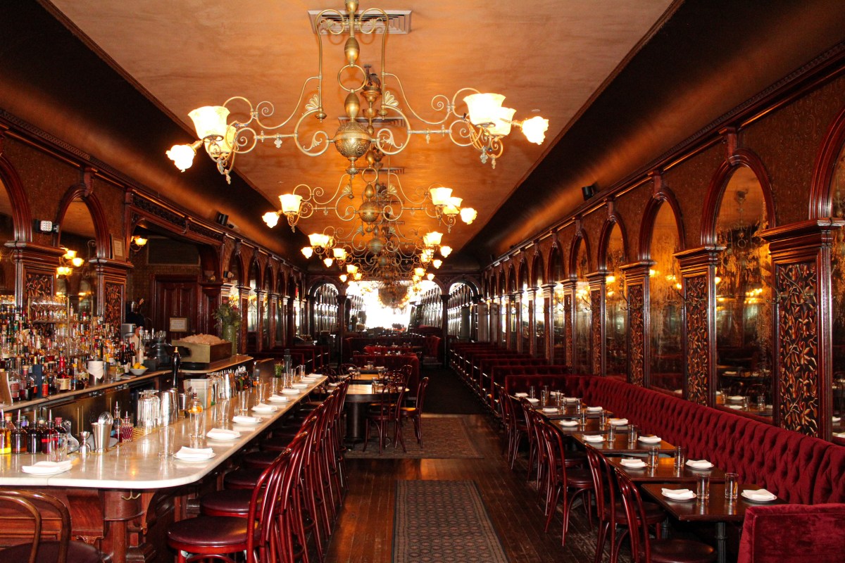 Ornate dining room interior with red velvet booths, brass chandeliers, mirrored arches, and long marble bar.