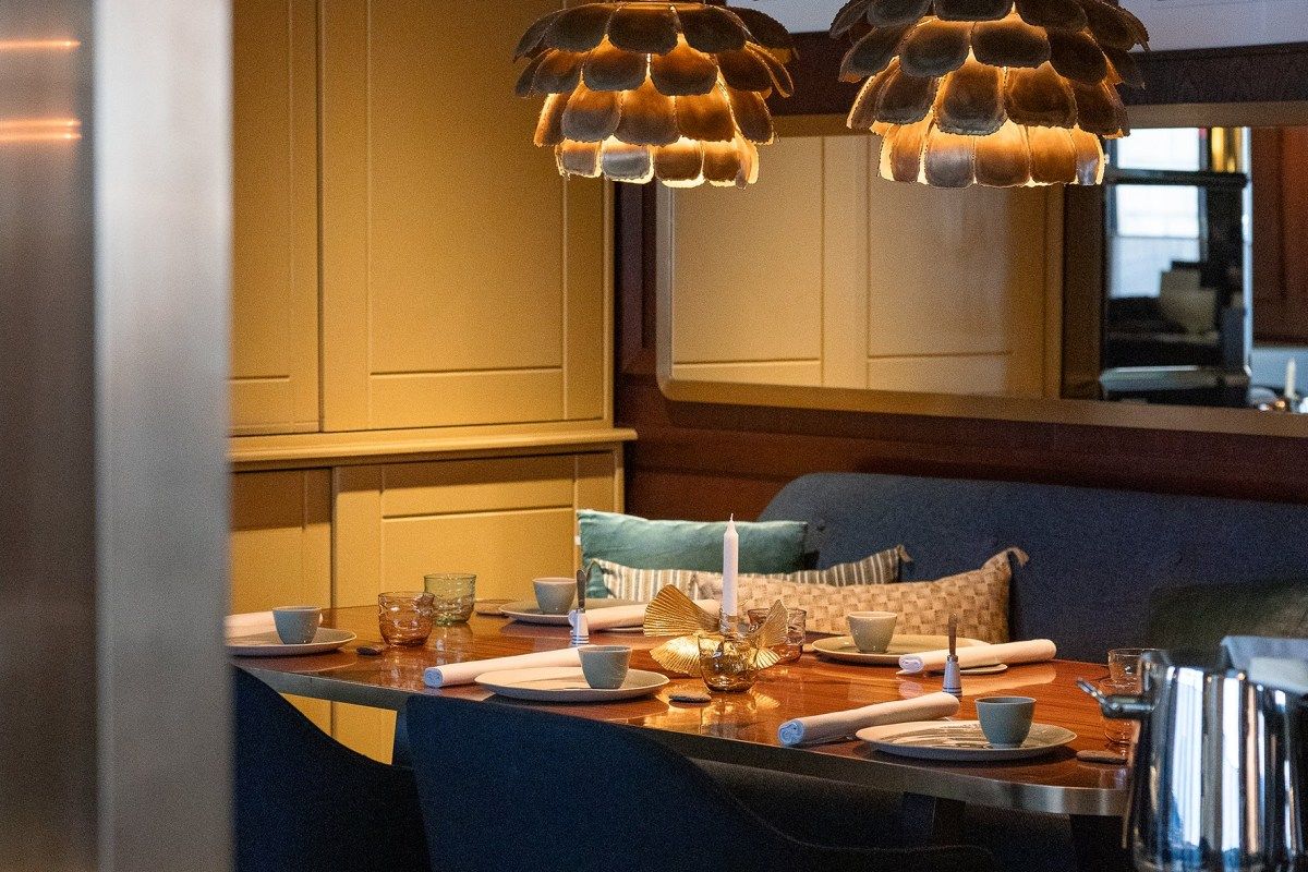 Elegant dining room corner with a wooden table set with blue plates, candle, and artichoke-shaped pendant lights