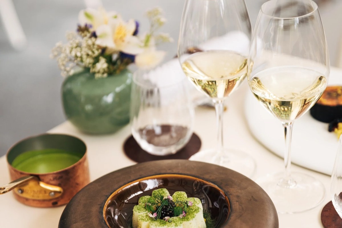 Elegant table setting with a plated dish, two glasses of white wine, flowers, and a small copper pot.