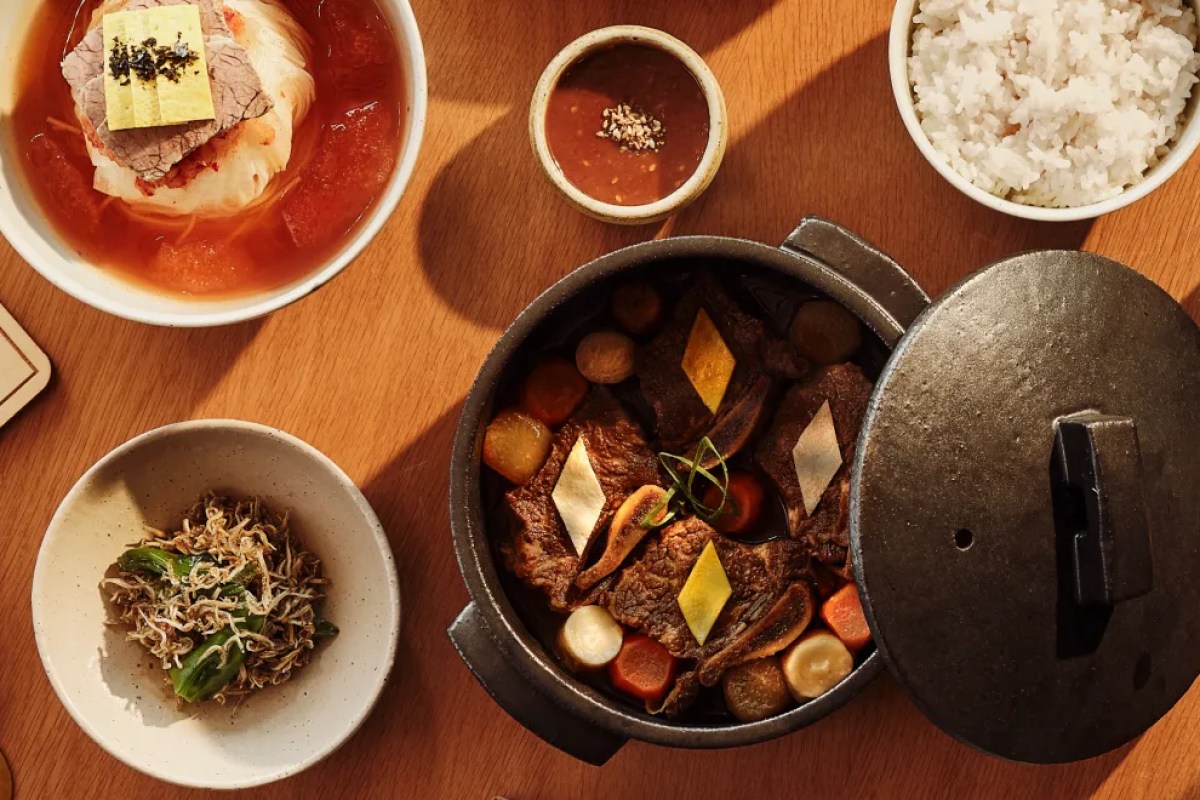 Korean dinner spread with a braised beef pot, soup, rice, dipping sauce and side dishes on a wooden table