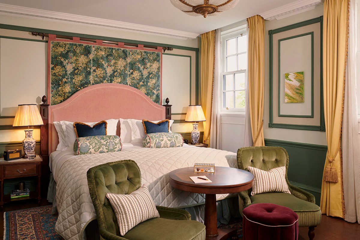 Guest bedroom with pink headboard, floral tapestry panel, green tufted chairs and yellow curtains