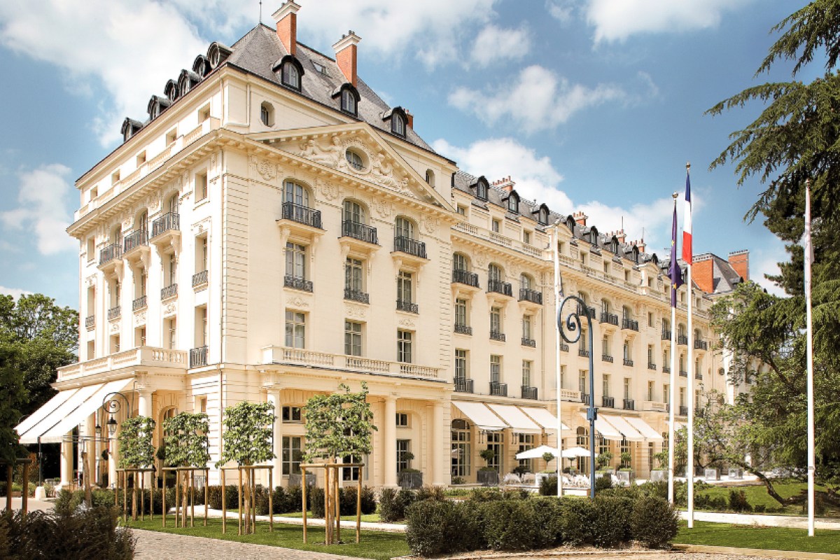 Front exterior view of the elegant cream stone Trianon Palace building with mansard roofs, balconies and French flags