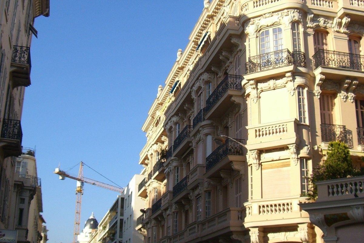 Ornate cream-colored Belle Époque building facade with balconies on Rue Gounod, Nice, under blue sky