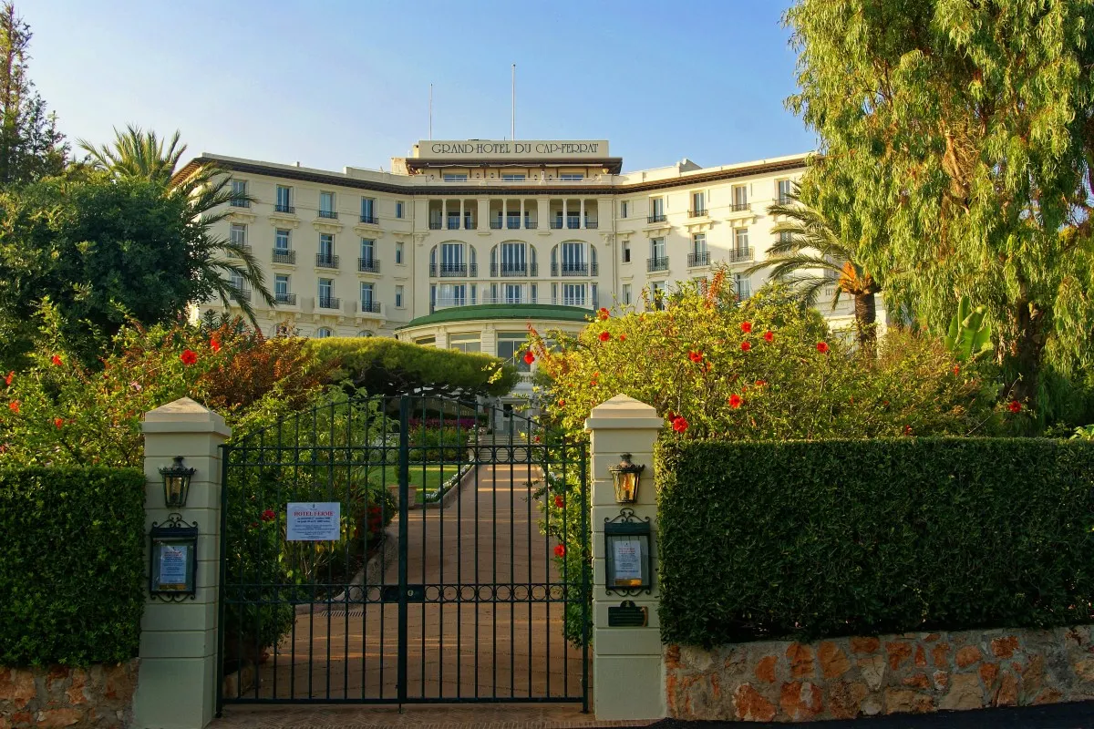 Grand-Hôtel du Cap-Ferrat façade seen through wrought-iron garden gate, framed by lush greenery and flowers