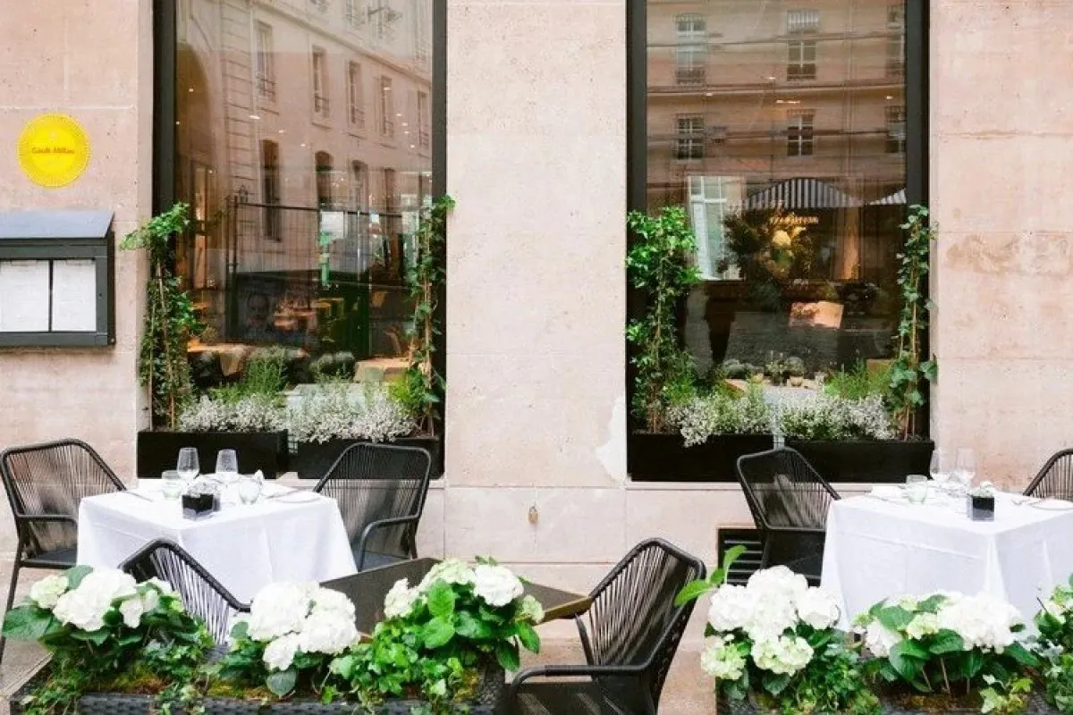 Outdoor terrace dining area with white-clothed tables, black chairs, and hydrangea flowers against stone facade