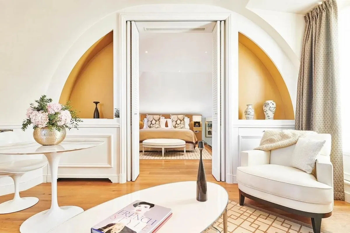 Elegant suite with arched alcoves, white armchair, coffee table, and view into bedroom