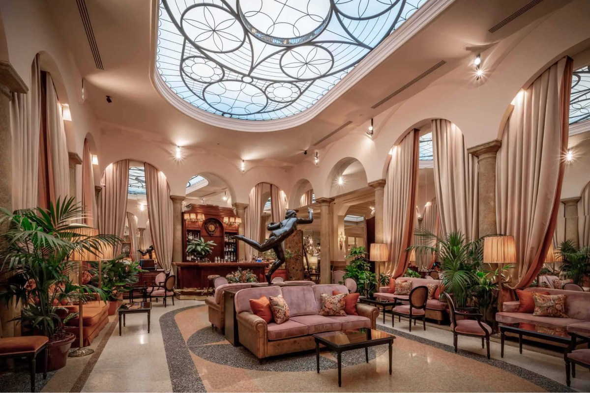 Grand hotel lounge with skylight, dancer statue, pastel sofas, and bar area