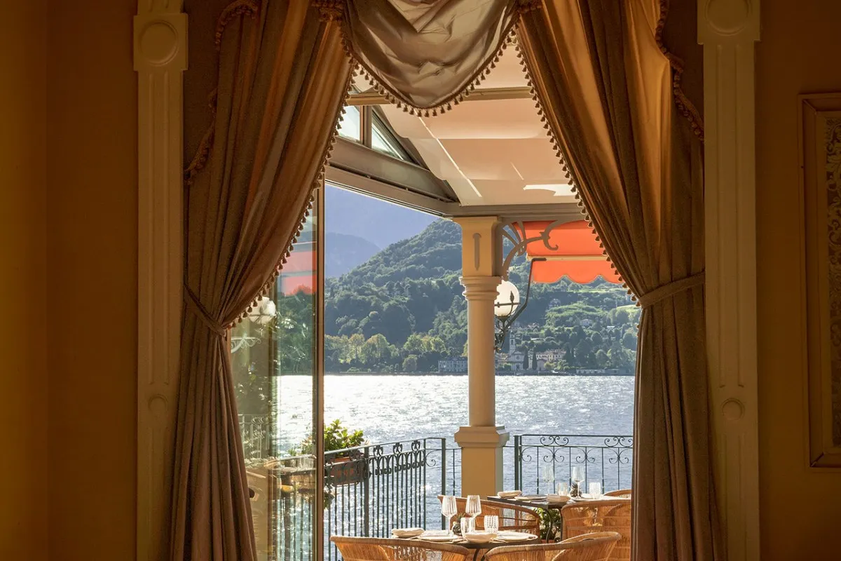 Restaurant terrace framed by curtains, overlooking Lake Como with set tables