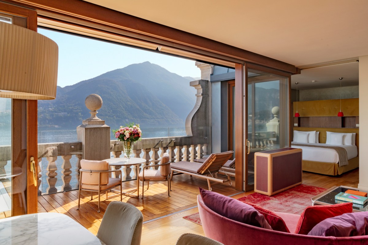 Guest suite with lake and mountain view through open glass doors, bed and seating area