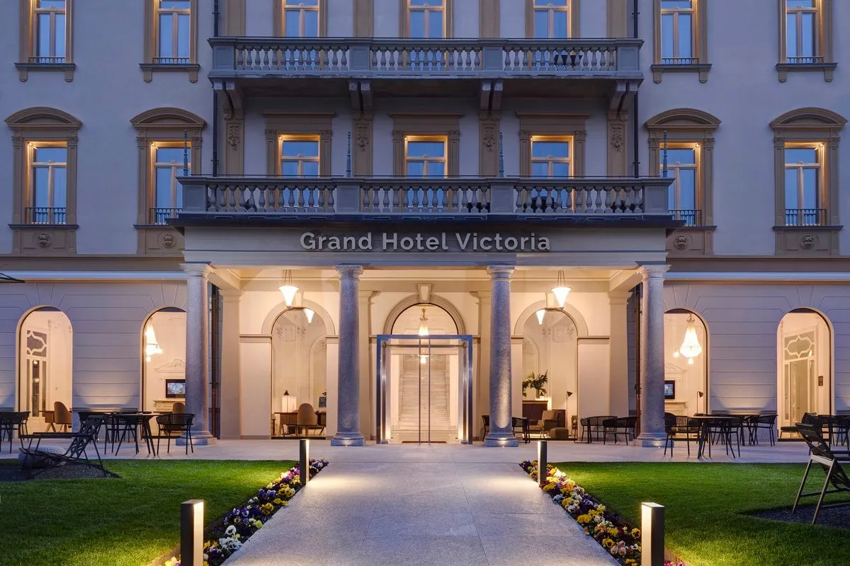 Evening facade of Grand Hotel Victoria with lit entrance, columns, balconies and manicured garden path