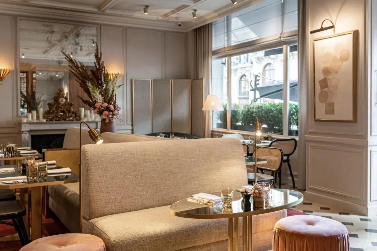 Elegant hotel lounge/restaurant interior with cream sofas, gold accents, and large window