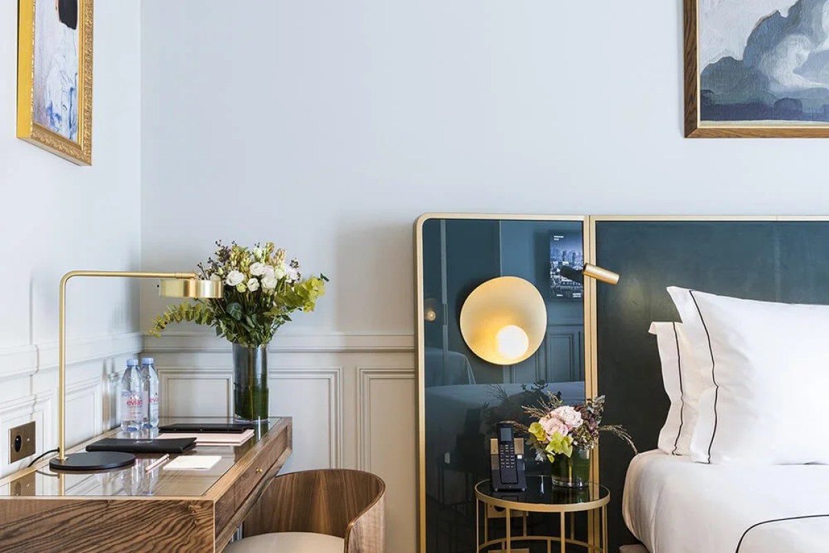 Hotel guest room corner with bed, nightstand, desk, lamp, and flowers