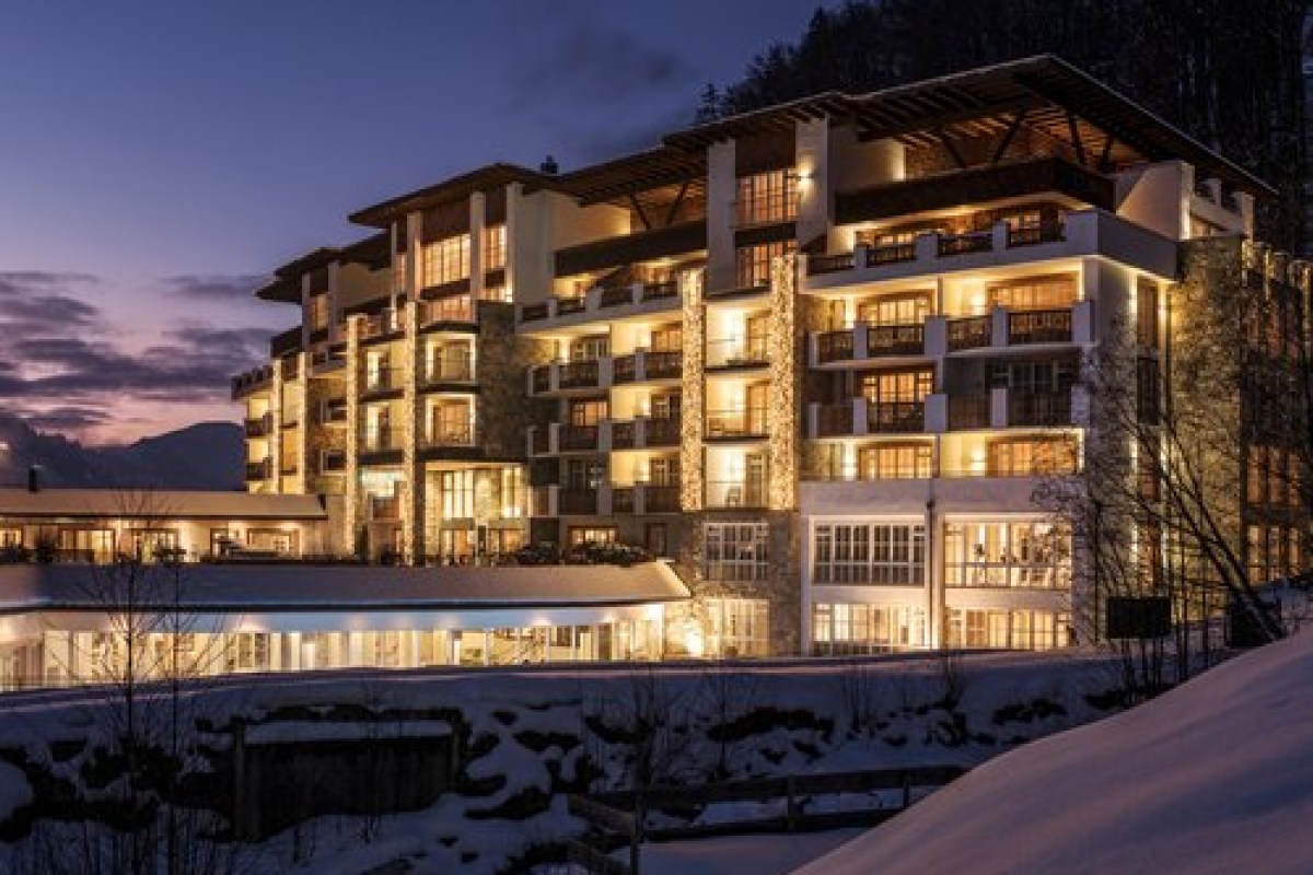 Grand Tirolia Kitzbühel hotel exterior illuminated at dusk, snowy mountain setting