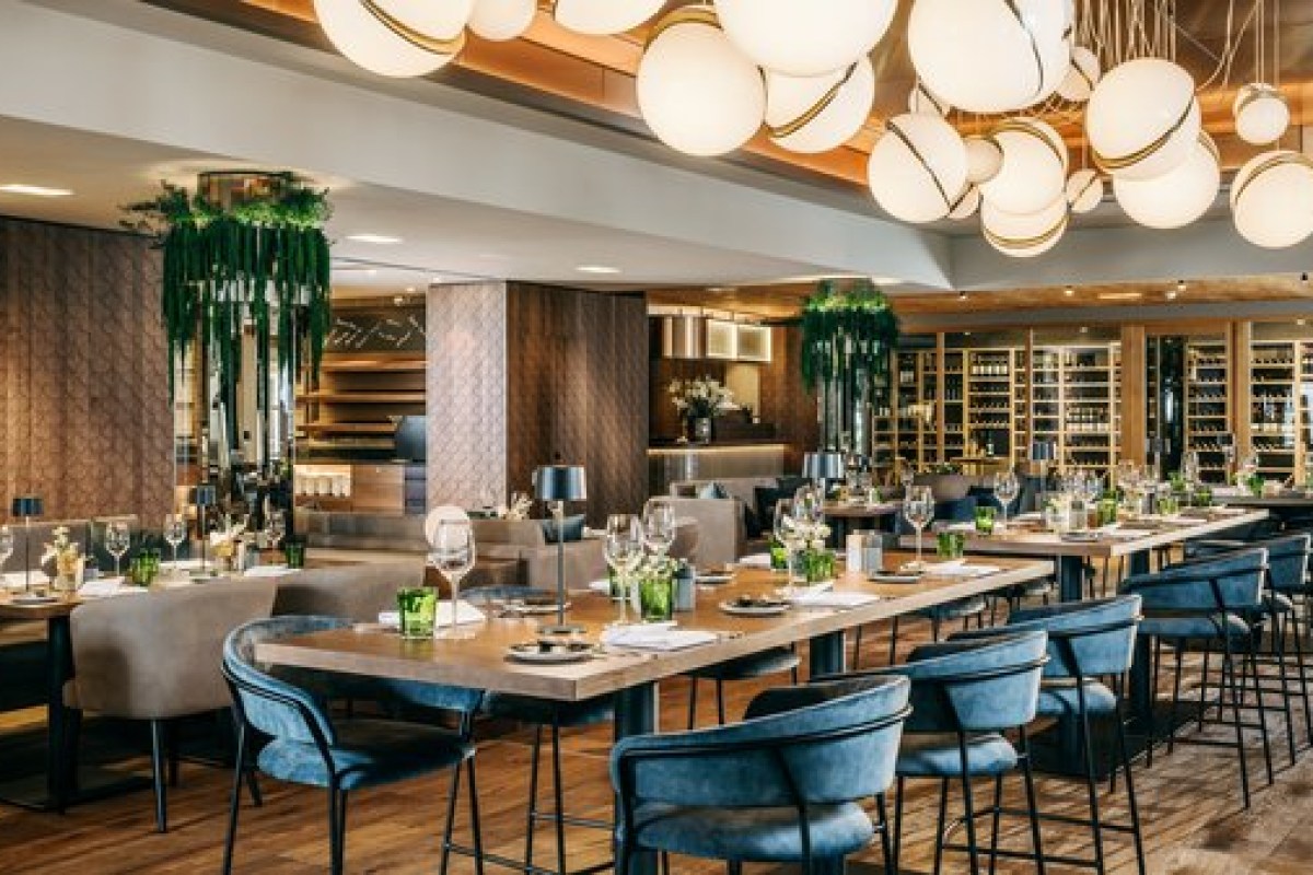Modern hotel restaurant with globe pendant lights, wood tables, blue chairs and wine display.
