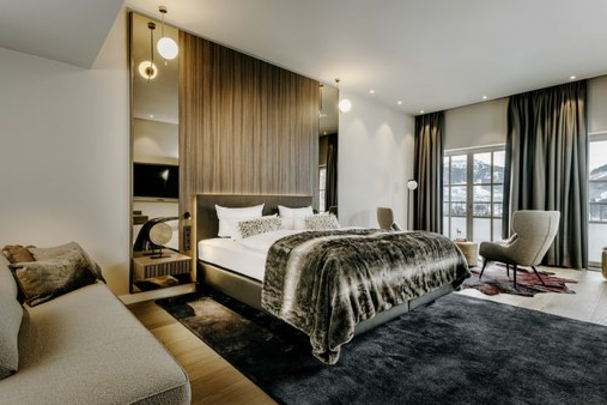 Spacious hotel bedroom with large bed, fur throw, mirrored headboard and mountain-view windows.