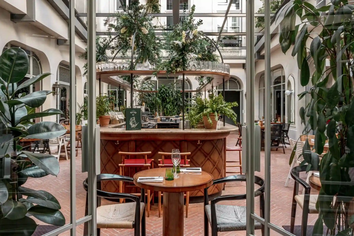 Interior courtyard with glass roof, greenery, wooden bar and dining tables