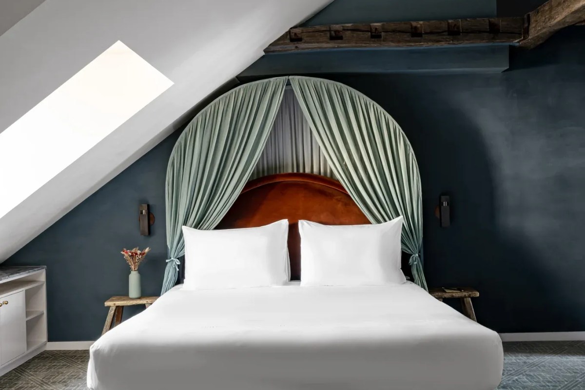 Guest room bed with curved orange headboard framed by sage green curtains under wooden beams