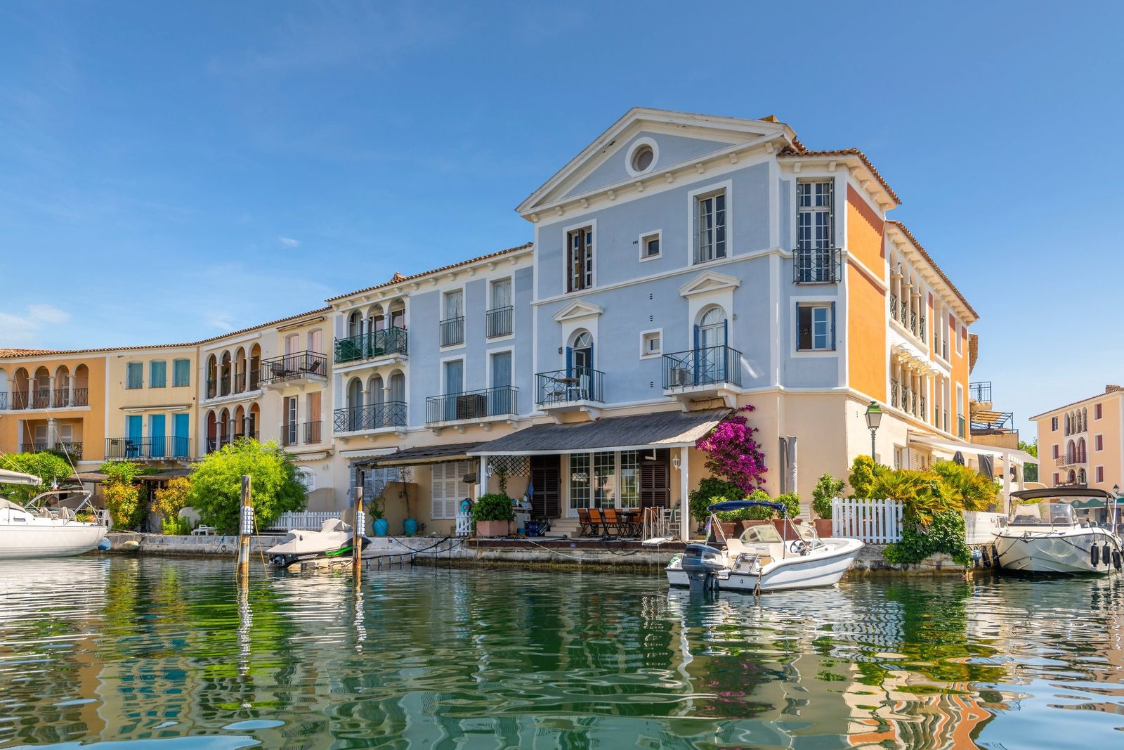 Pastel houses with balconies and bougainvillea on a canal in Port Grimaud, with motorboats moored at the doors