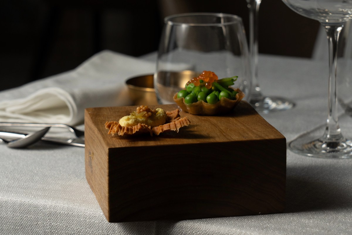 Tasting bites on a wooden block: pea tart with roe, cracker with cream, at a set table