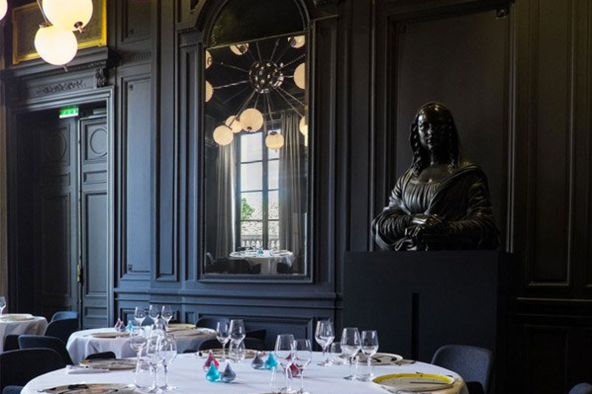 Elegant dark-paneled dining room with black bust sculpture, mirror and chandelier reflection, set tables with wine glasses