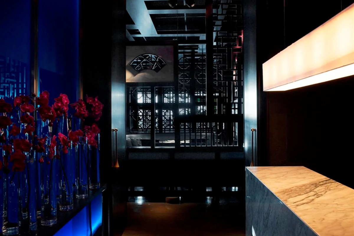 Dark restaurant entrance with marble host stand and red orchids beside a patterned screen