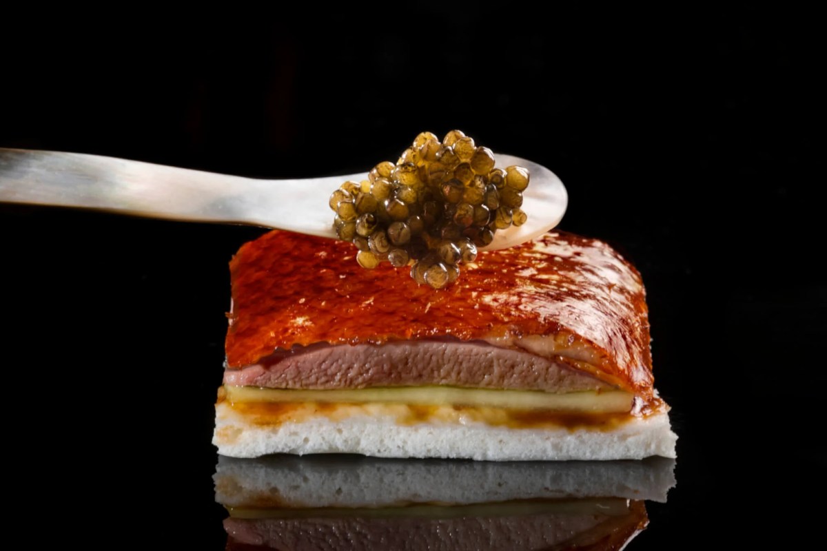 Elegant appetizer of crispy duck and foie gras topped with caviar on a glossy black surface