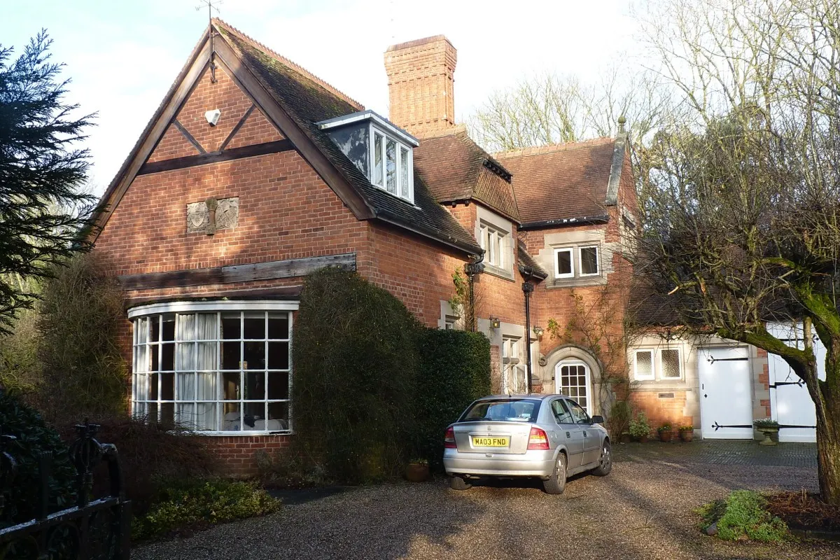 Red brick Arts and Crafts style cottage with gabled roof, chimneys and gravel driveway, part of the Hampton Manor estate in Hampton-in-Arden