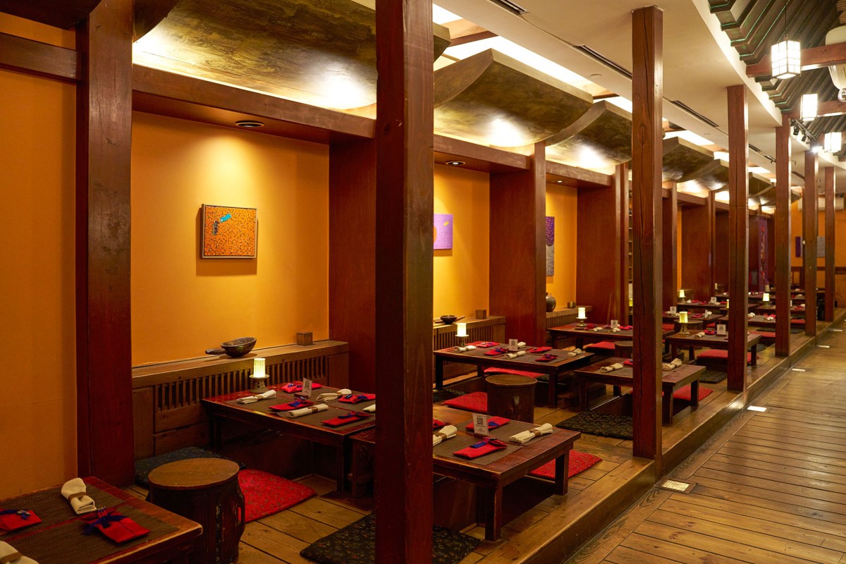 Dining room with wooden booths, low tables set with red napkins and cushions