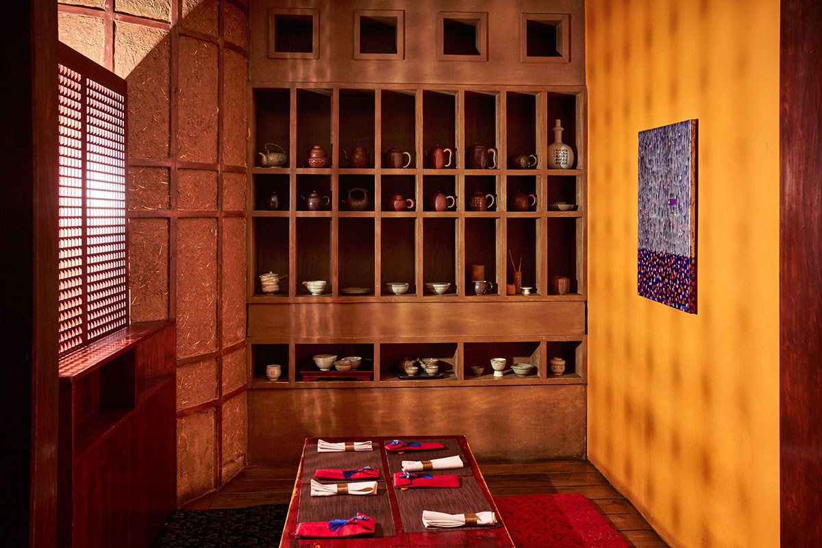 Cozy dining nook with traditional shelving of pottery, low table set for guests, warm lighting