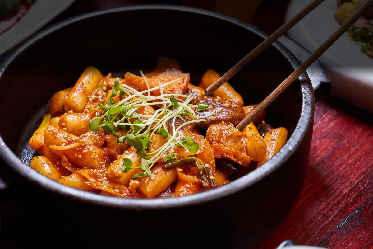 Stone pot of spicy rice cakes (tteokbokki) with chopsticks, garnished with microgreens