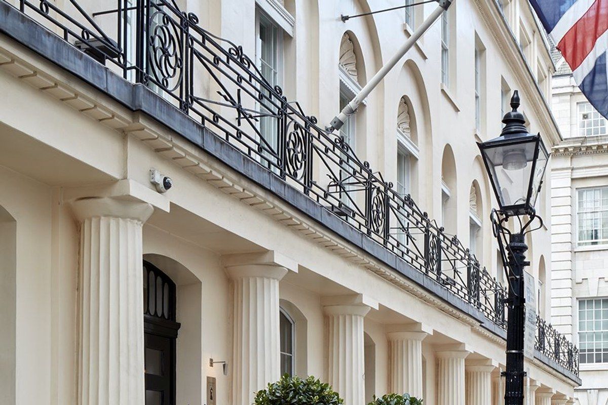 Angled view of the hotel's cream façade with Ionic columns, wrought-iron balcony railings and a street lamp