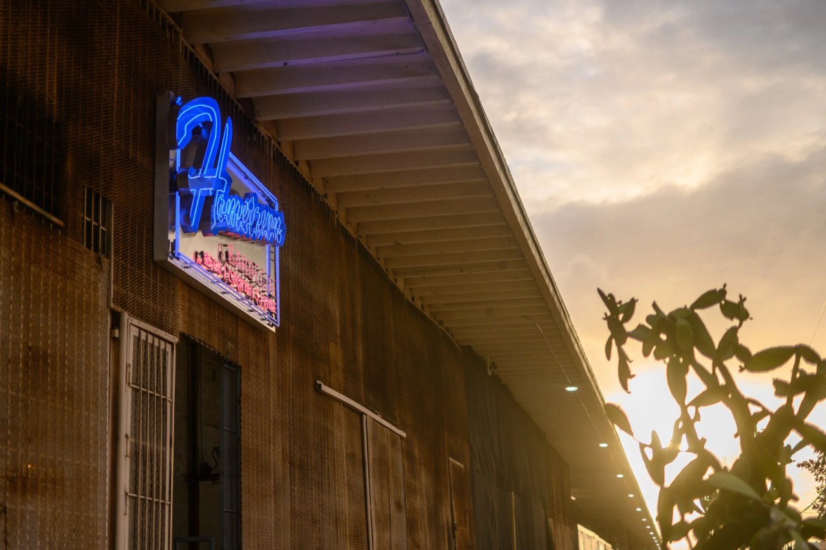 Restaurant exterior with illuminated neon 'Hometown' sign at dusk, metal facade and greenery