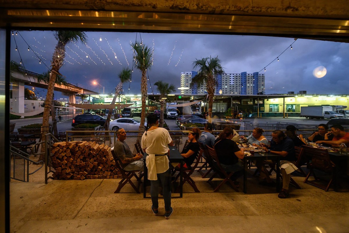 Outdoor terrace dining area with string lights, palm trees and diners at tables at dusk