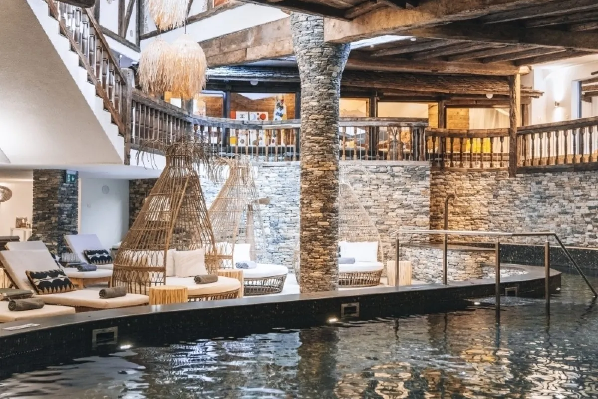 Indoor spa pool area with stone columns, wooden balconies, and woven lounge chairs.