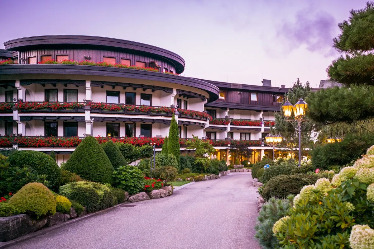Hotel Bareiss building exterior at dusk with illuminated facade, balconies with red flowers, and garden path
