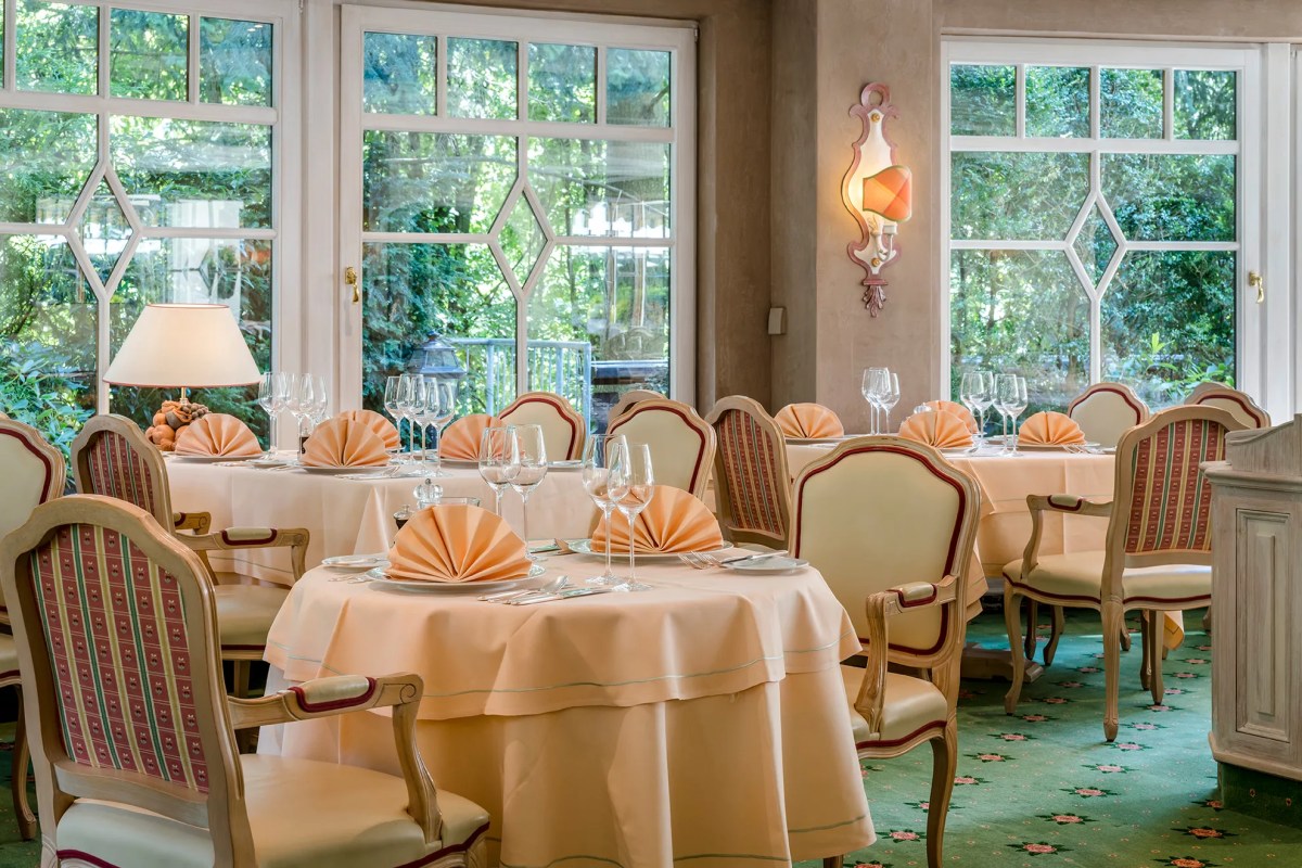 Elegant hotel restaurant with set tables, peach napkins, and garden view through tall windows